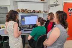 Cztery kobiety stoją przed monitorem omawiając temat. Jedna kobieta siedzi przed komputerem.