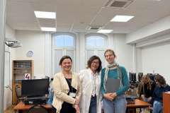 Trzy kobiety stoją w sali z komputerami i uśmiechają się. Z tyłu siedzą dwie młode kobiety, patrzą się na podłogę