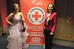 dwie kobiety stoją, w tle ścianka promocyjna, jedna kobieta trzyma w ręku skrzypce