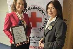 dwie kobiety stoją na tle ścianki promocyjnej, jedna trzyma w rękach dyplom