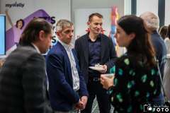 Kilka osób rozmawia podczas przerwy kawowej na wydarzeniu; mężczyzna w garniturze trzyma filiżankę na spodku i prowadzi rozmowę z innymi uczestnikami