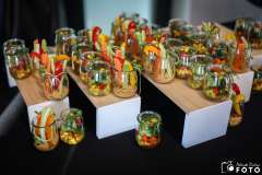 Małe szklane słoiczki ustawione na podestach z przekąskami z surowych warzyw – m.in. marchewki, selera, papryki i brokułów – podane podczas cateringu