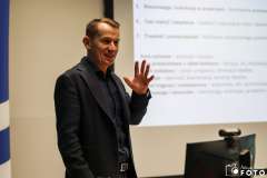 Mężczyzna prowadzi prezentację w sali szkoleniowej, stojąc obok ekranu z wyświetlonym slajdem 