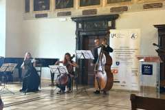 trzy osoby w starodawnej sali gra na instrumentach muzycznych