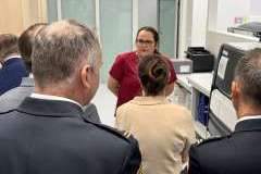 Grupa dorosłych osób stoi w pomieszczeniu i ogląda otoczenie, jedna kobieta mówi