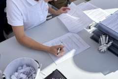 Młoda kobieta siedząca na krześle przy stoliku pochylona nad dokumentem który wypełnia