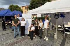 Grupa kobiet i mężczyzn przed przygotowanym stoiskiem uczelni i namiotem ochronnym