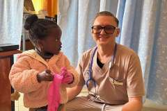 Mężczyzna w uniformie medycznym kuca przy małej dziewczynce, mężczyzna uśmiecha się