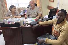 trzy osoby siedzące przy biurku, dwie w uniformach medycznych