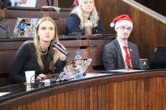 młoda kobieta w czapce mikołaja siedzi na auli konferencyjnej i mówi przez mikrofon