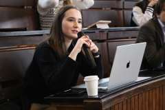 młoda kobieta w czapce mikołaja siedzi na auli konferencyjnej i mówi przez mikrofon