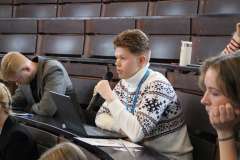 młody mężczyzna siedzi na auli konferencyjnej i mówi przez mikrofon