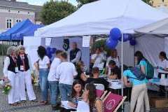 Grupa kobiet i mężczyzn podczas prezentacji na stoisku uczelni i namiotem ochronnym