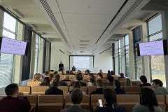 Uczestnicy siedzą na sali wykładowej i oglądają prezentację wyświetlaną na ekranie