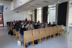 Uczestnicy siedzą w sali wykładowej i słuchają prezentacji