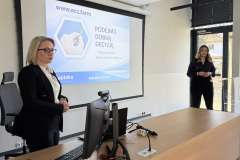 Dwie kobiety stoją w sali wykładowej przed ekranem z prezentacją