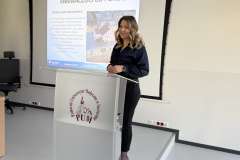 Kobieta stoi przy mównicy z logo PUM i przemawia na tle slajdu prezentacji