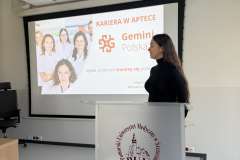 Kobieta stoi przy mównicy z logo PUM i przemawia na tle slajdu prezentacji