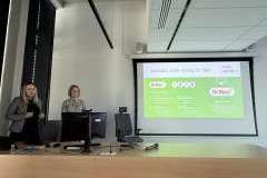 Dwie kobiety stoją w sali wykładowej przed ekranem z prezentacją