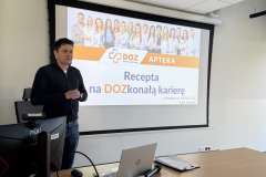 Mężczyzna stoi przy mównicy z logo PUM i przemawia na tle slajdu prezentacji