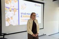 Kobieta stoi przy mównicy z logo PUM i przemawia na tle slajdu prezentacji