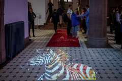 Na podłodze holu wyświetlona projekcja zebry prowadzi w stronę czerwonego dywanu z logo PUM; w tle widać uczestników wydarzenia