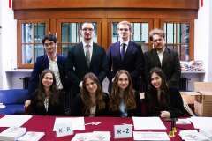 Osiem osób pozujących do zdjęcia za stołem rejestracyjnym; na blacie leżą listy z oznaczeniami literowymi K–P i R–Ż oraz materiały konferencyjne