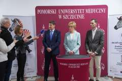 Dziennikarka z mikrofonem rozmawia z trojgiem przedstawicieli uczelni stojących przed ścianką z logo PUM w Szczecinie