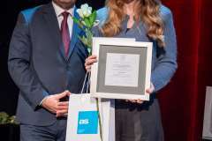 kobieta i mężczyzna stojący na scenie, kobieta trzyma w rękach różę, dyplom oraz torbę