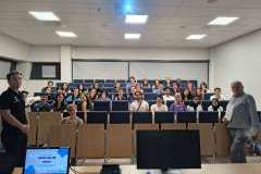 Grupa młodych, uśmiechniętych ludzi w sali wykładowej z wykładowcą