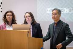 Trzy osoby stoją przy mównicy i prowadzą prezentację podczas spotkania naukowego