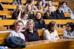 Uczestniczki siedzą w auli wykładowej i rozmawiają ze sobą przed spotkaniem. Dwie inne uśmiechają się do obiektywu