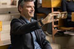 mężczyzna siedzi w auli wykładowej, robi zdjęcie telefonem, w tle uczestnicy wykładu