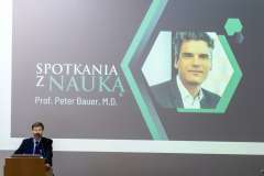 mężczyzna stojący przy mównicy, w tle slajd z wykładu