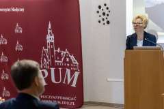 kobieta stojąca przy mównicy, w tle ścianka promocyjna PUM
