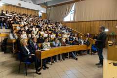 uczestnicy wykładu siedzą na sali wykładowej, przed nimi stoi mężczyzna