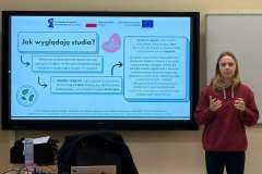 kobieta stoi obok ekranu z prezentacją zatytułowaną „Jak wyglądają studia?” i wykonuje gest rękami podczas wystąpienia.