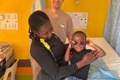 młody mężczyzna w uniformie medycznym stoi przy łóżku szpitalnym z kobietą. na łóżku siedzi dziecko, uśmiechają się