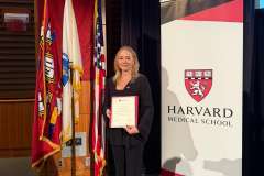 kobieta stojąca przed ścianką promocyjną , trzyma w ręku dyplom