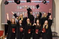 Absolwenci w czarnych togach podrzucają birety w górę podczas uroczystości