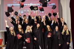 Absolwenci w czarnych togach podrzucają birety w górę podczas uroczystości