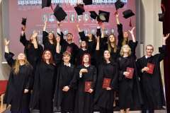 Absolwenci w czarnych togach podrzucają birety w górę podczas uroczystości