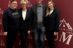 cztery uśmiechnięte osoby stoją przed ścianką promocyjną