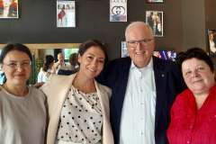 Trzy stojące kobiety i jeden mężczyzna na tle ściany na której wiszą kolorowe zdjęcia 