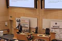 Prelegent stoi przy mównicy przed uczestnikami zjazdu