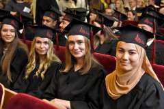 Uroczystość absolutoryjna. Grupa siedzących studentów w togach i biretkach