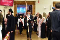 Uroczystość absolutoryjna. Poczet wchodzi do auli. Student wnosi sztandar uczelni