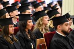 Uroczystość absolutoryjna. Grupa siedzących studentów w togach i biretkach