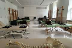 Sala warsztatowa z łózkami rehabilitacyjnymi oraz z modelem kręgosłupa leżącym na ławce z przodu