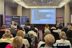 Zdjęcie przedstawia konferencję medyczną, prelegent mówi przez mikrofon i pokazuje slajd, uczestnicy siedzą i słuchają prezentacji.